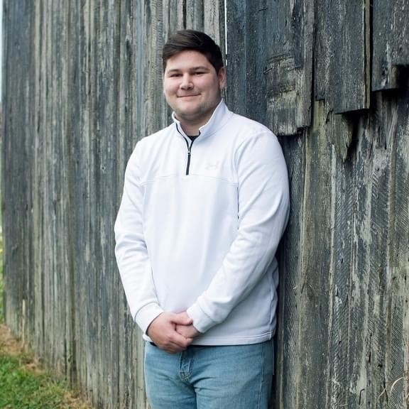 Peyton Knight smiles for the camera outside against a wood fence