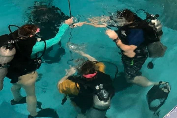 Student club members practice diving in a swimming pool.