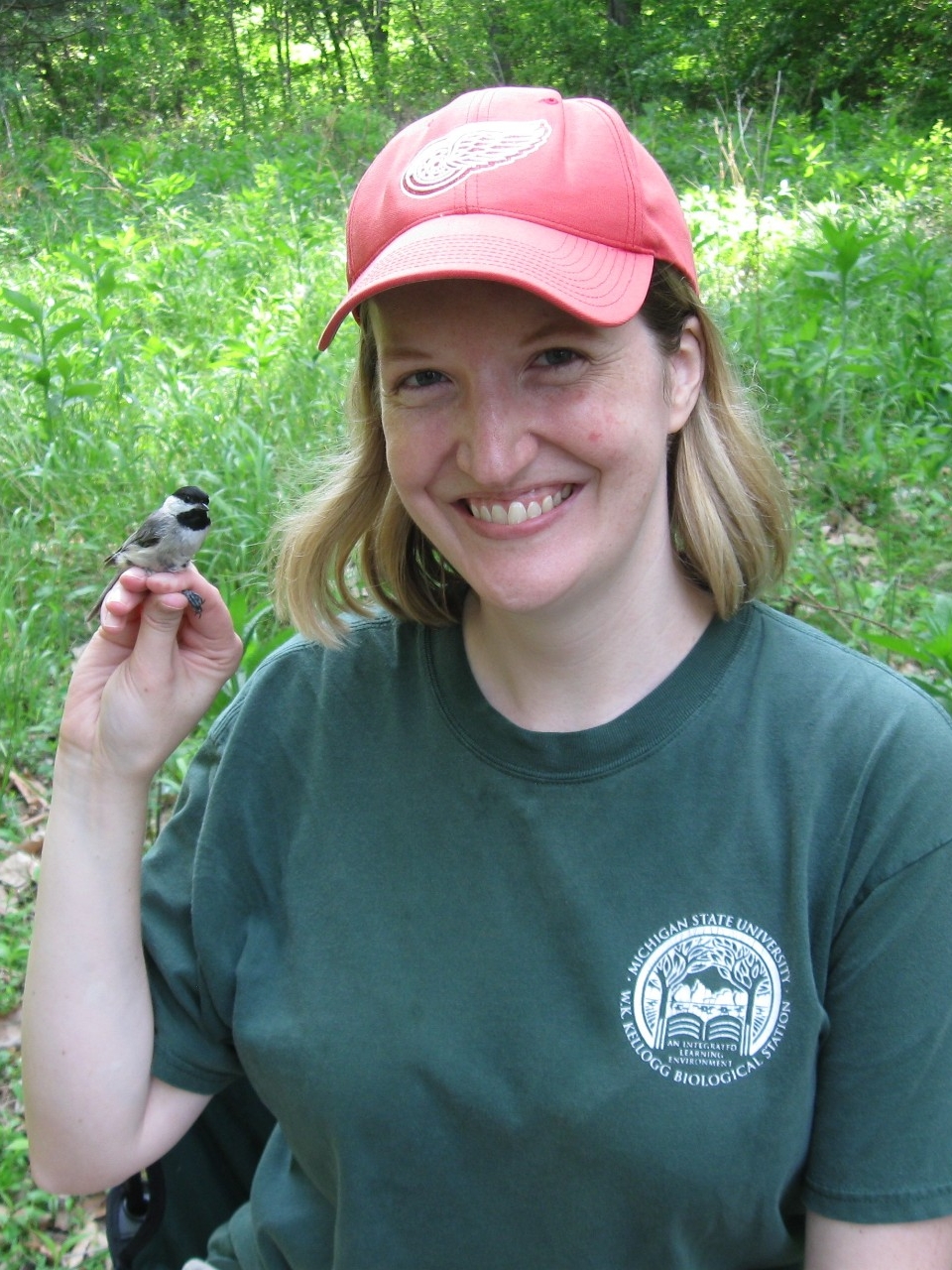 Photo of Dr. Walters, outside in a grassy area, with a small bird sitting on her fingers.
