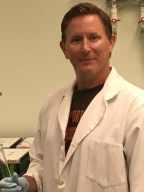 Photo of Dr. Thompson, in a lab setting, wearing a lab coat.