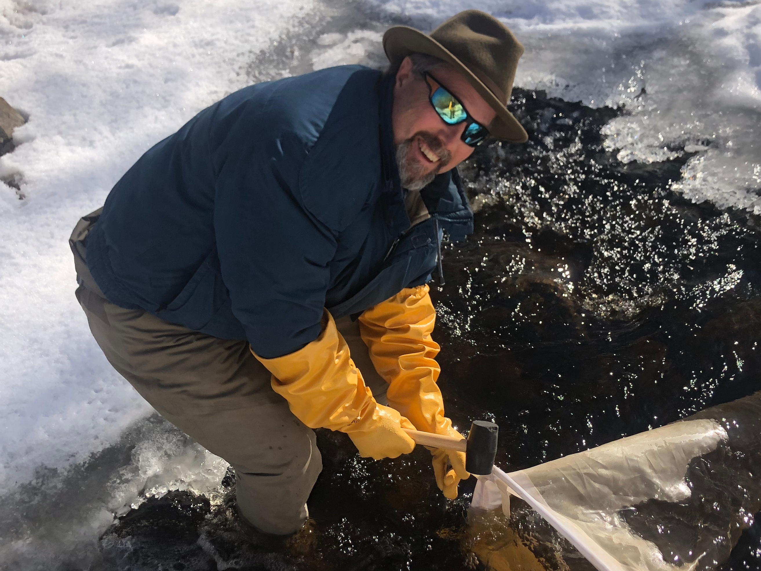 Photo of Dr. Durtsche outside. He appears to be on a mountaintop, hammering a marker into the ground. 