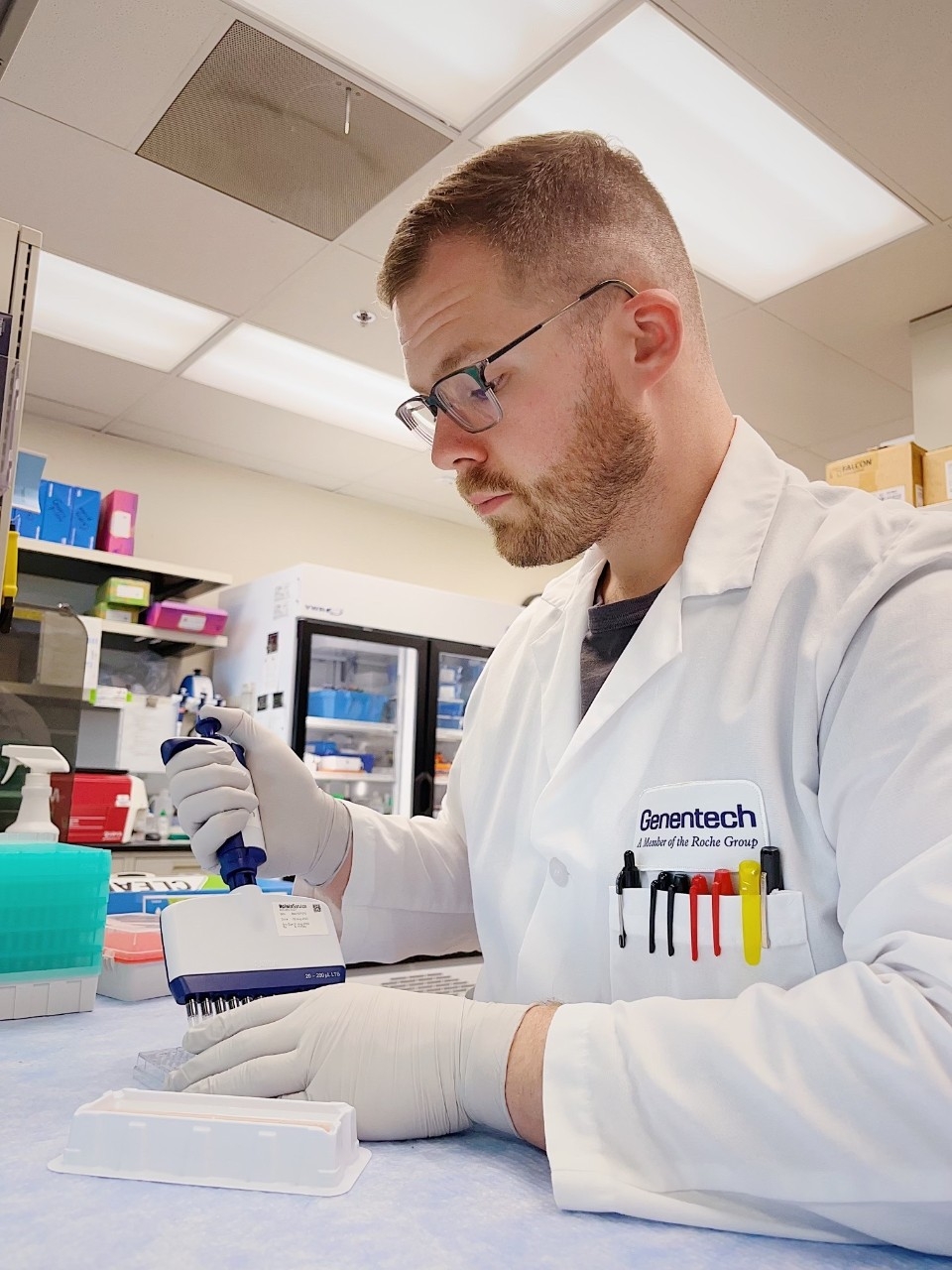 Justin Gibson conducst laboratory research in a white lab coat and gloves.