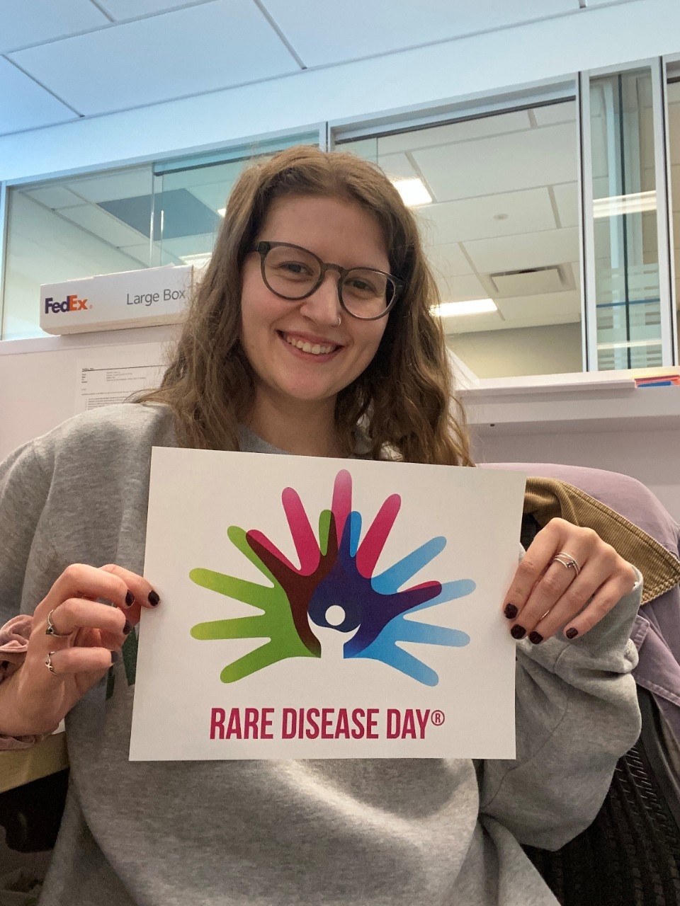 Sara Steffen smiles while holding up a sign that says "Rare Disease Day".