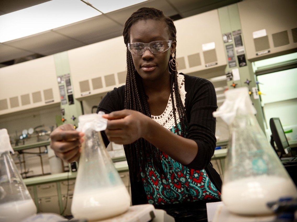 Student wearing protective goggles, working with lab beakers