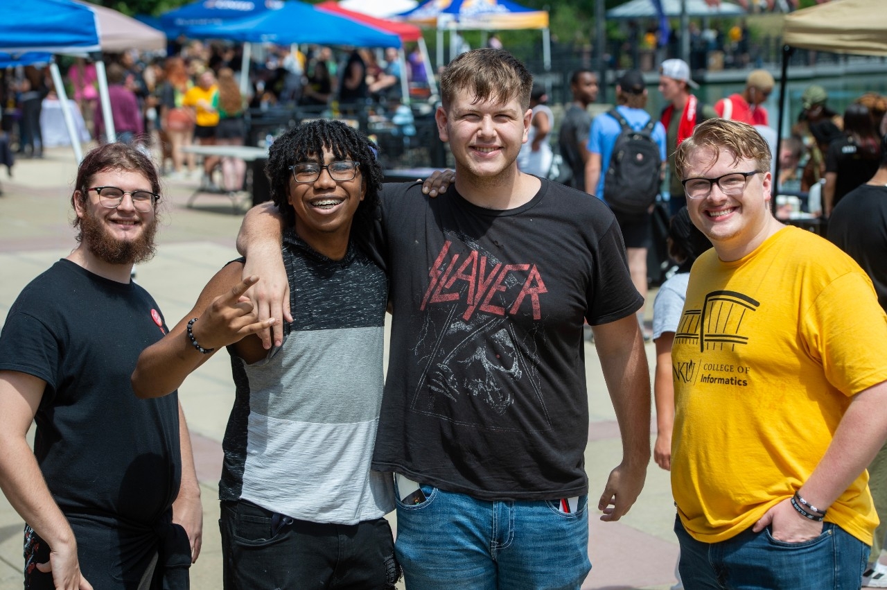 Four male students standing together at Victorfest. One student with his arm around another.