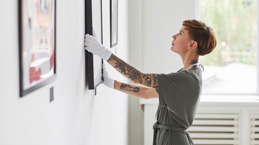 Side view portrait of woman hanging paintings on wall while planning art gallery exhibition