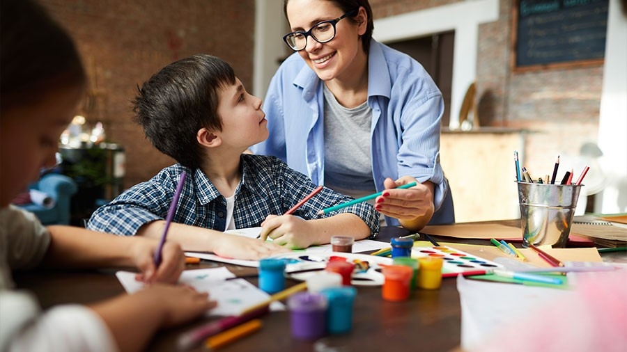 A teacher assists a student with painting and coloring with pencils